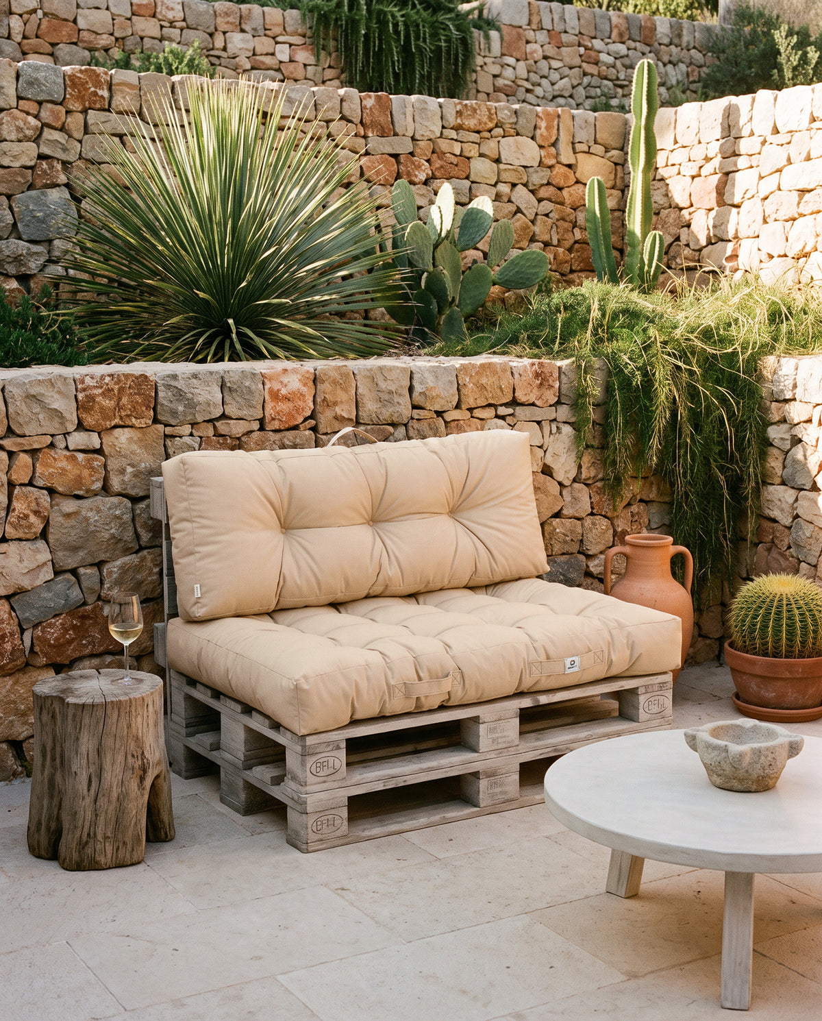 Cuscini per pallet capitonné beige Deco Arts su due pallet, davanti a muri a secco terrazzati