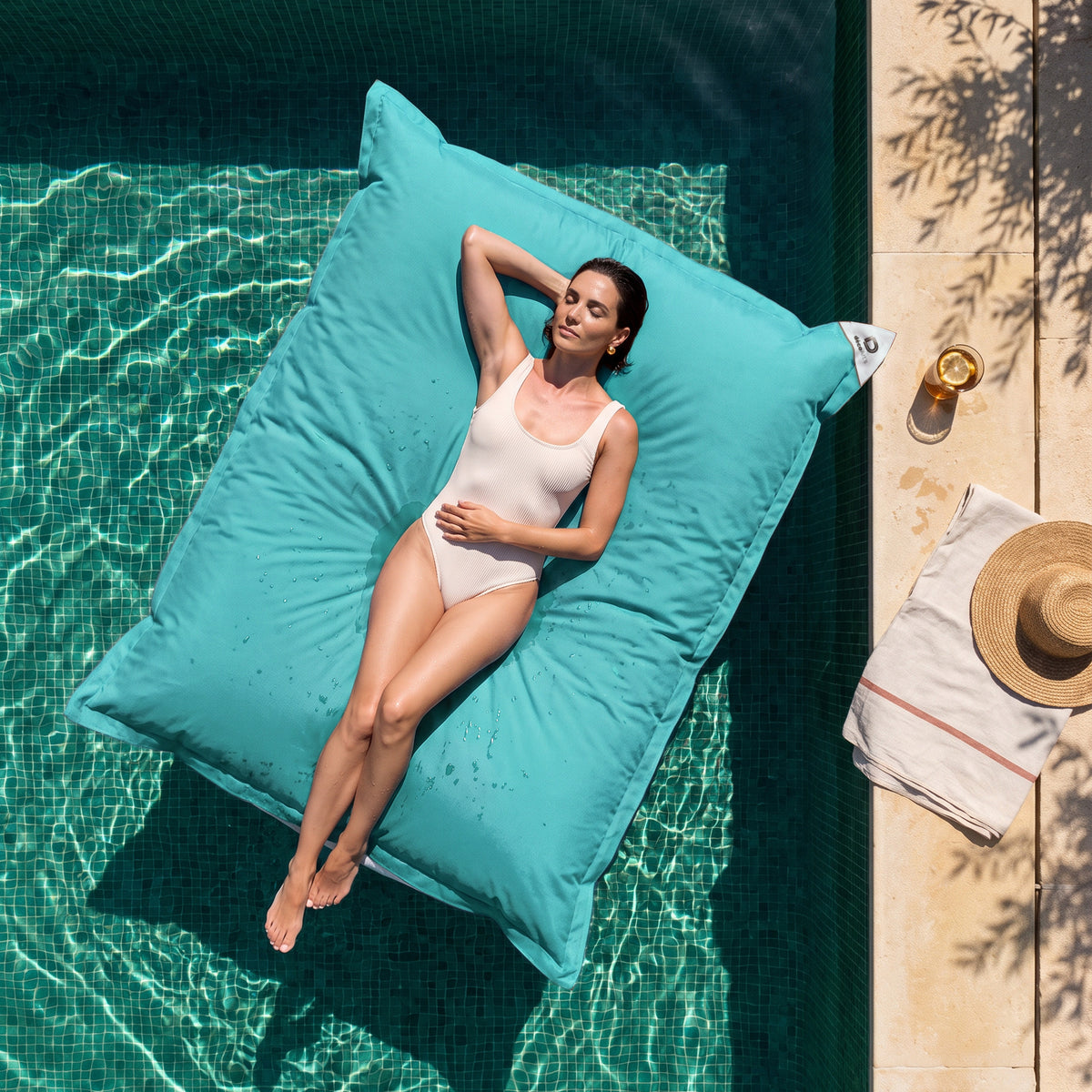 Solo fodera, da riempire – Pouf galleggiante gigante 180 × 140 cm Blu Caraibi in piscina, donna sdraiata al sole, vista dall'alto