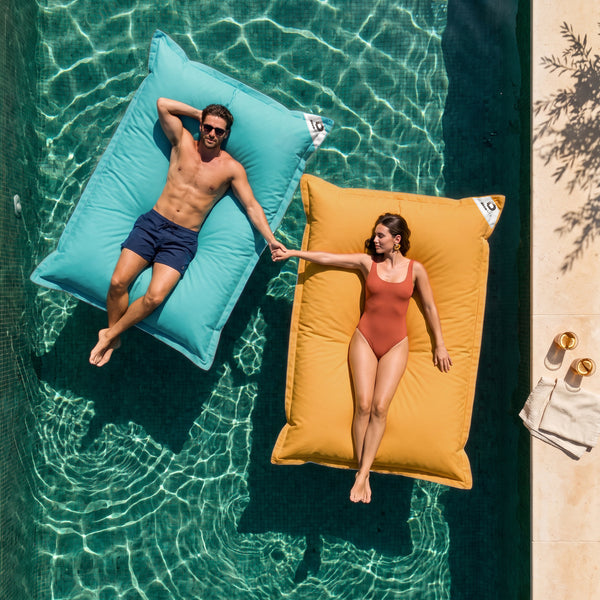 Solo fodera, da riempire – Due pouf galleggianti giganti Deco Arts, Blu Caraibi e Giallo Miele, in piscina con una coppia, vista dall'alto